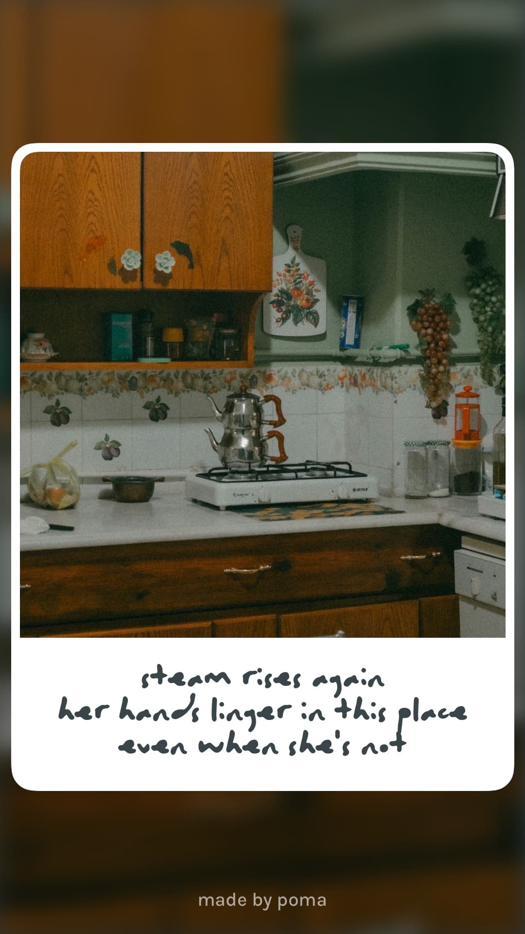 An old kitchen with a silver teapot on the stove, floral wallpaper, wooden cabinets