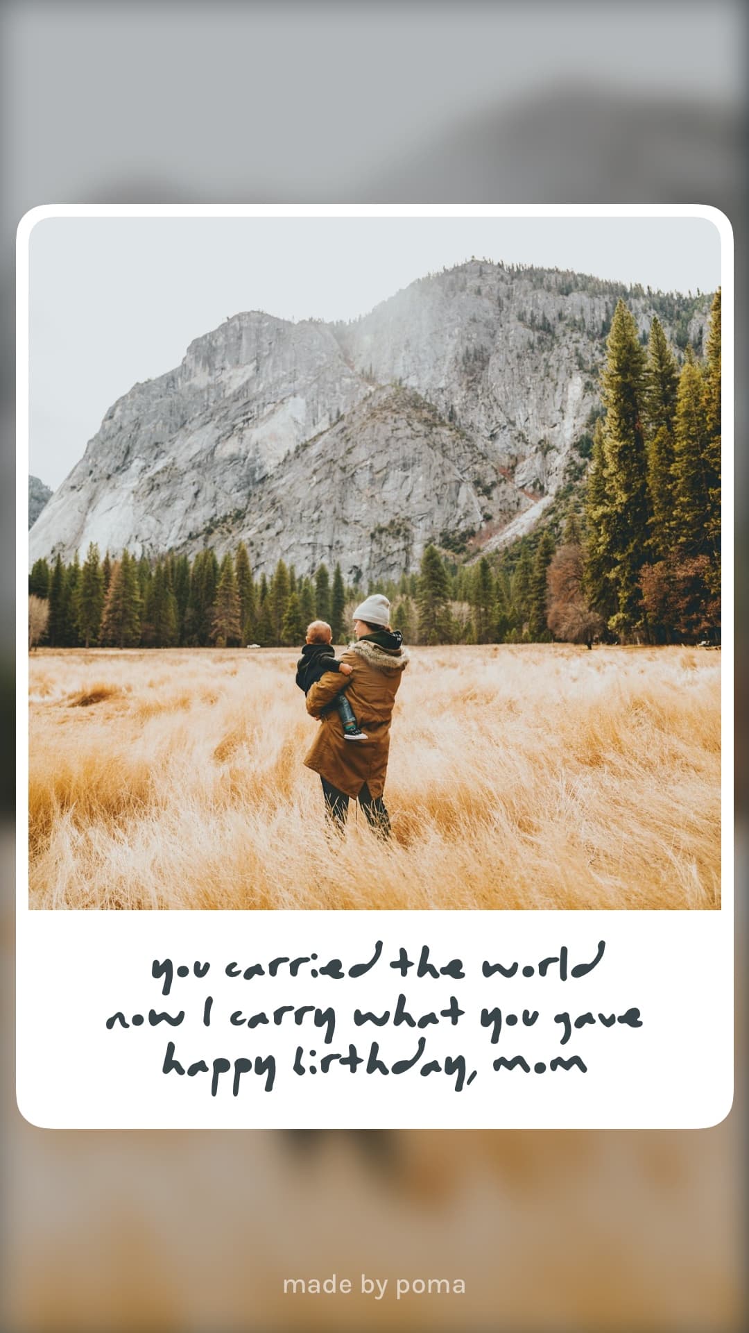 A mom carrying her child in a golden field with mountains behind